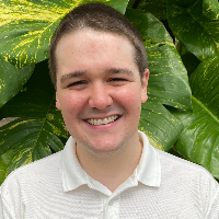Tyler standing in front of a tree, smiling, head shot.